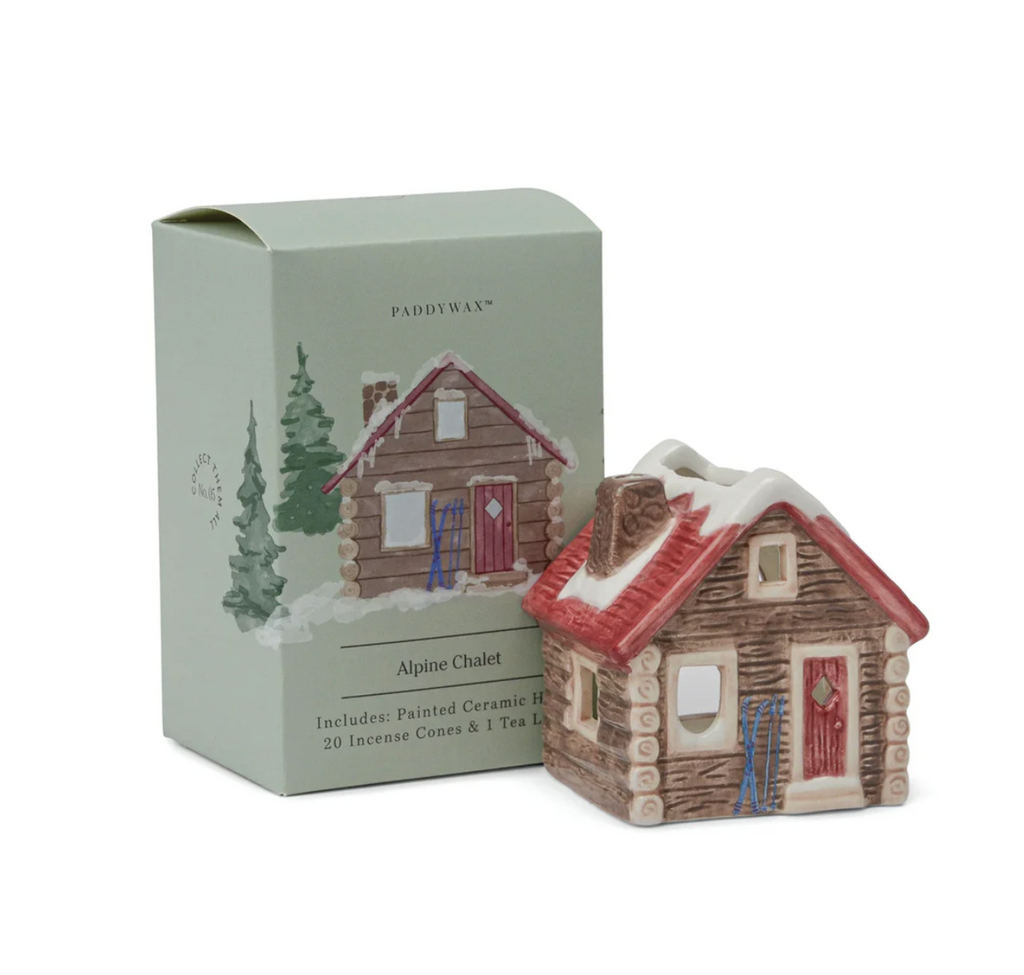 The Alpine Chalet ceramic tea light holder/ incense burner shaped like a rustic cabin with red snow covered roof set in front of the green box with illustrated drawing of the Alpine Chalet on the cover. 