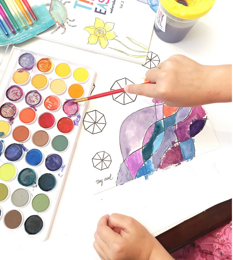 Child's hands using watercolor palette to paint on watercolor paper.