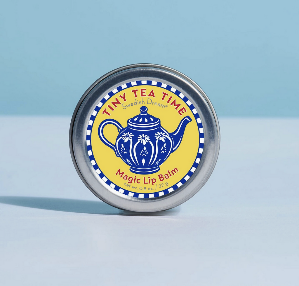 Round lip balm tin with a bright yellow and blue label featuring a teapot that reads Tiny Tea Time Magic Lip Balm