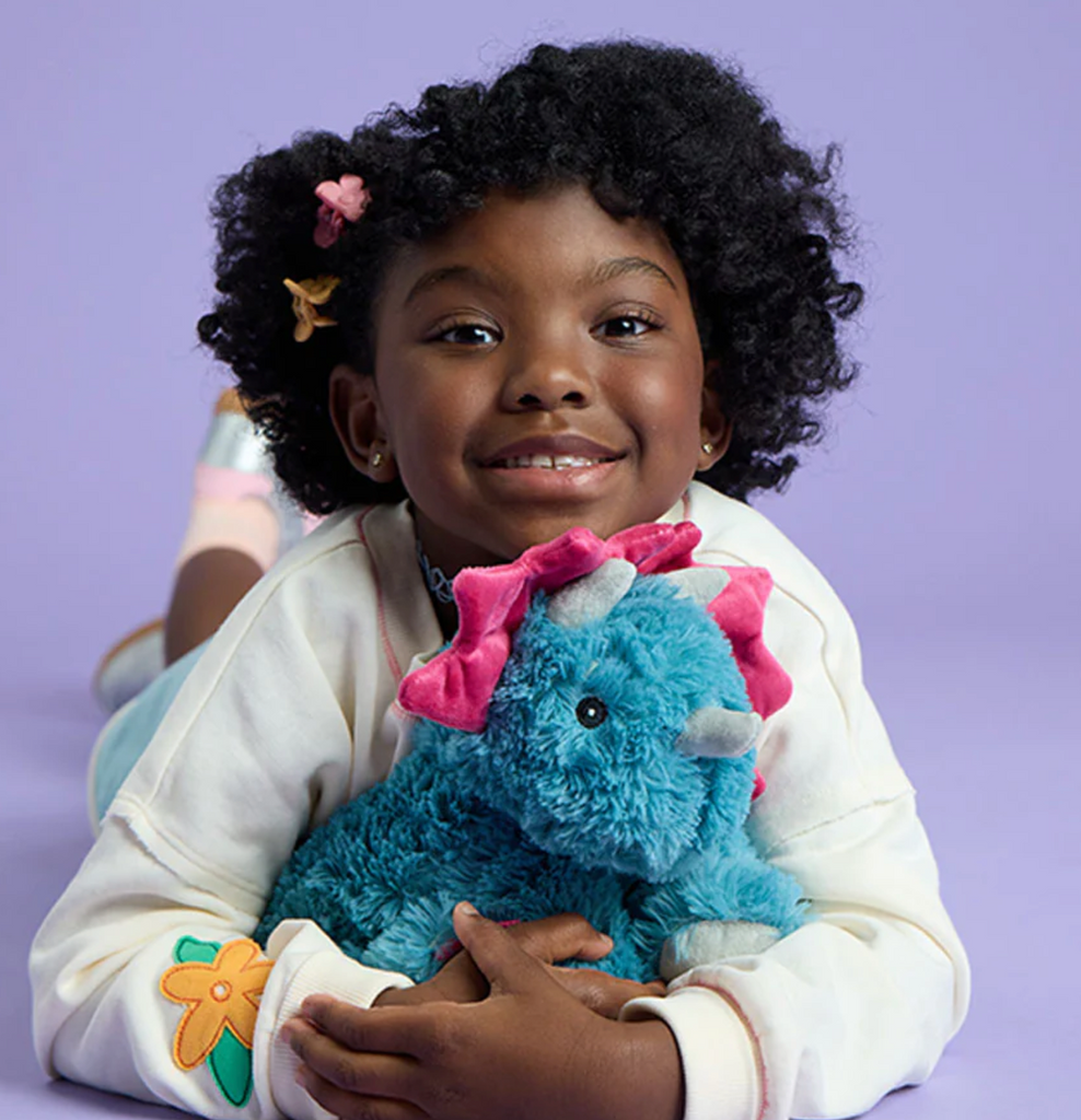 A young child laying on the floor hugging the Triceratops Warmies. 