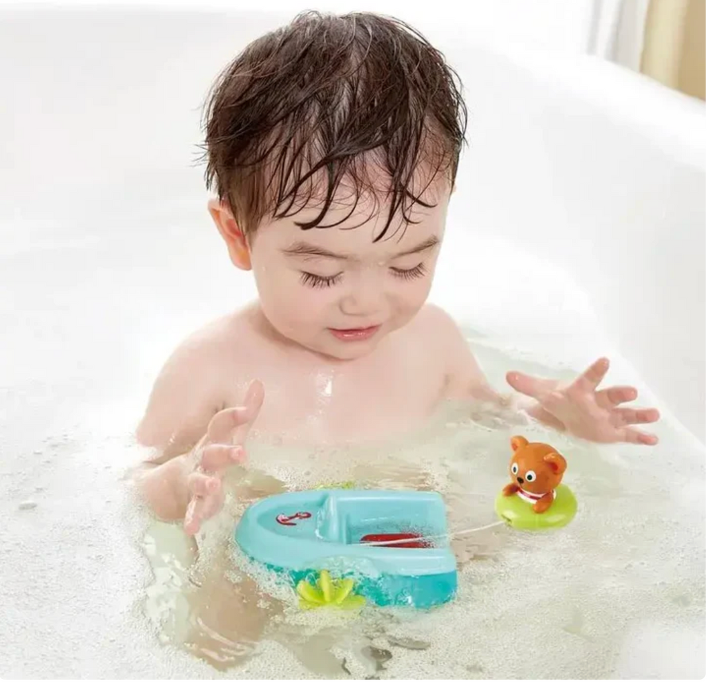 Child playing in a bathtub with bath toys, including a boat and a teddy bear in a float.