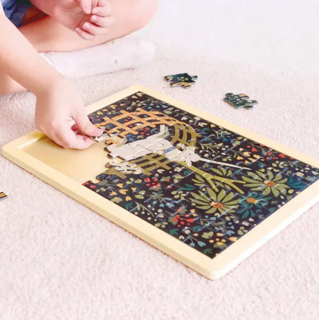 The Unicorn in a Garden puzzle being put together by a child sitting on the floor. 