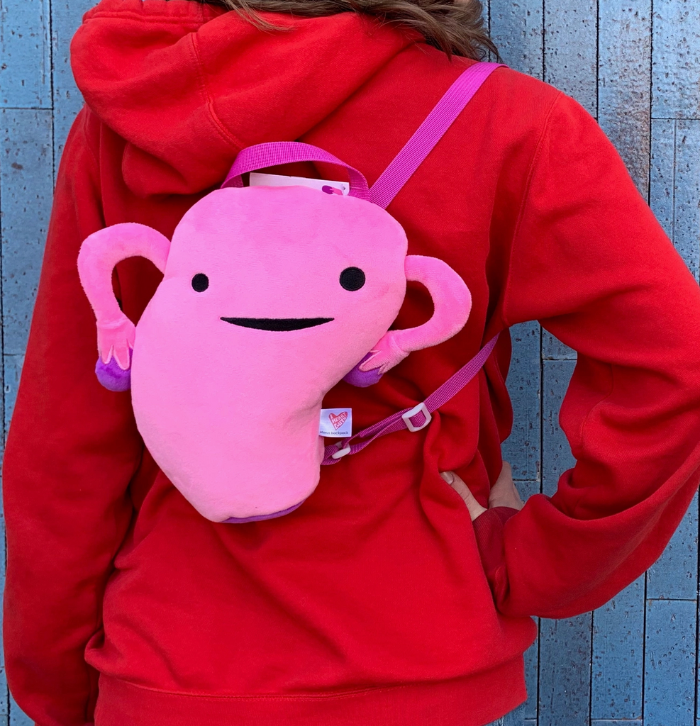 The pink Uterus backpack being worn by someone wearing a red hoodie.