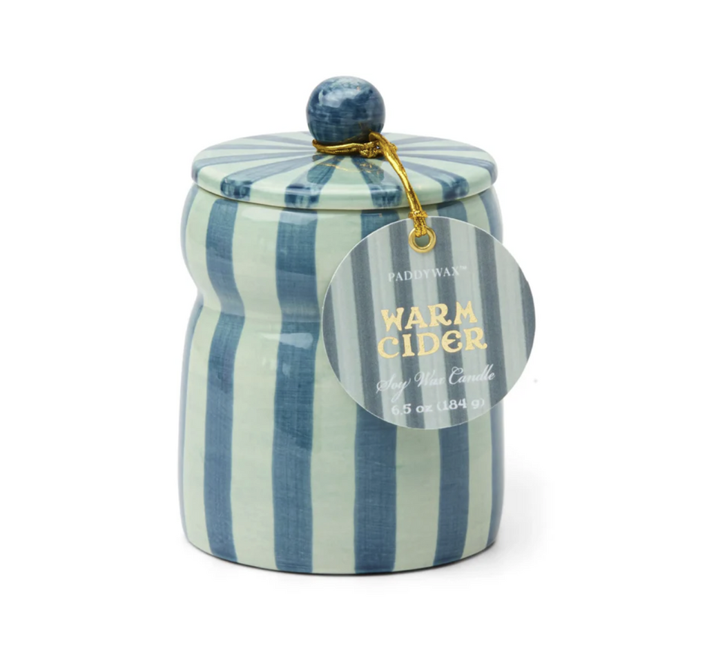 Scented candle in a ceramic hand-painted light blue and teal ceramic vessel with lid. There is a tag hanging from the top that reads "Warm Cider" Soy Wax Candle. 