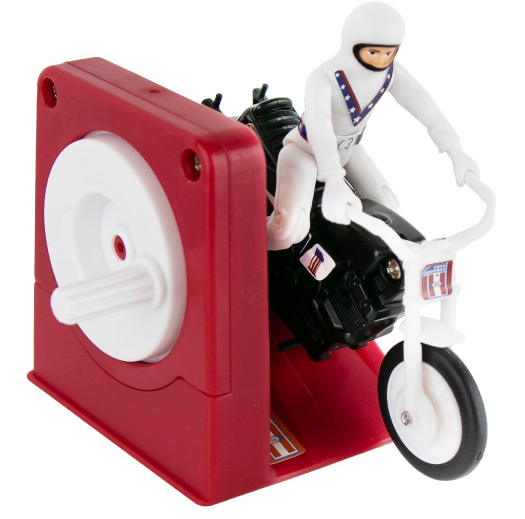 Toy figure of Evel Knievel  on a motorcycle with a red launching ramp with a hand crank. 