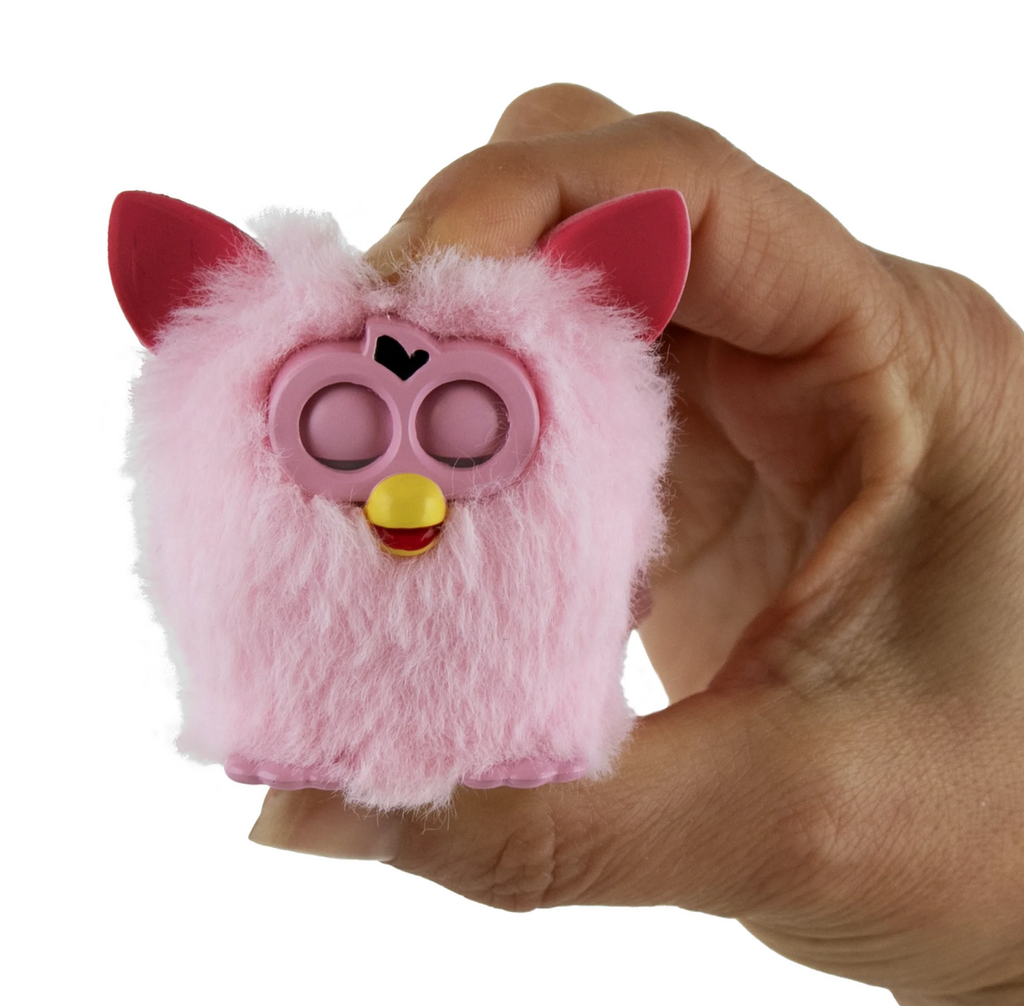 Pink fuzzy World's Smallest Furby with  red ears held in a hand to show the miniature scale. 