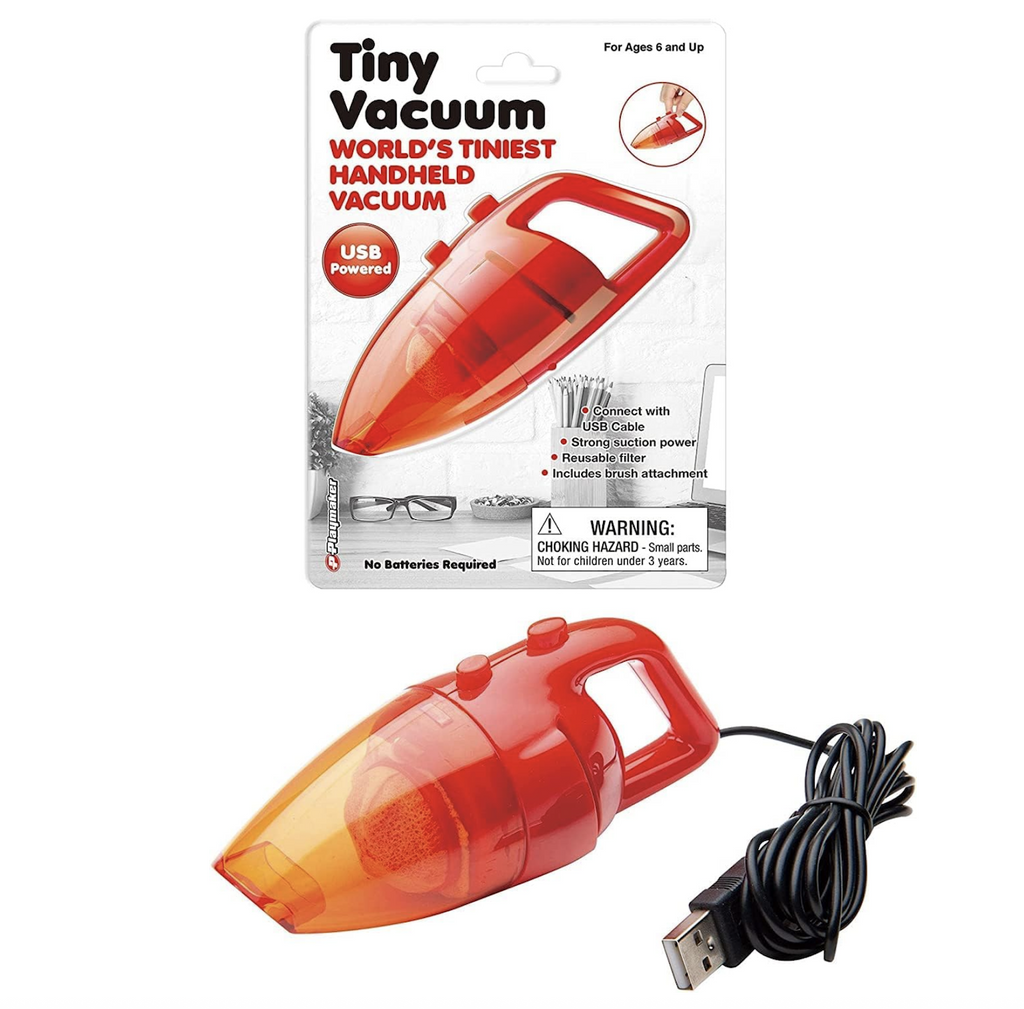 The World's Tiniest Vacuum, an orange, miniature handheld vacuum with the charging cord attached. It is set in front of the packaging it comes in with a colorful card that has the vacuum pictured above a desk that has a cup of pencils, glasses and computer on it. 