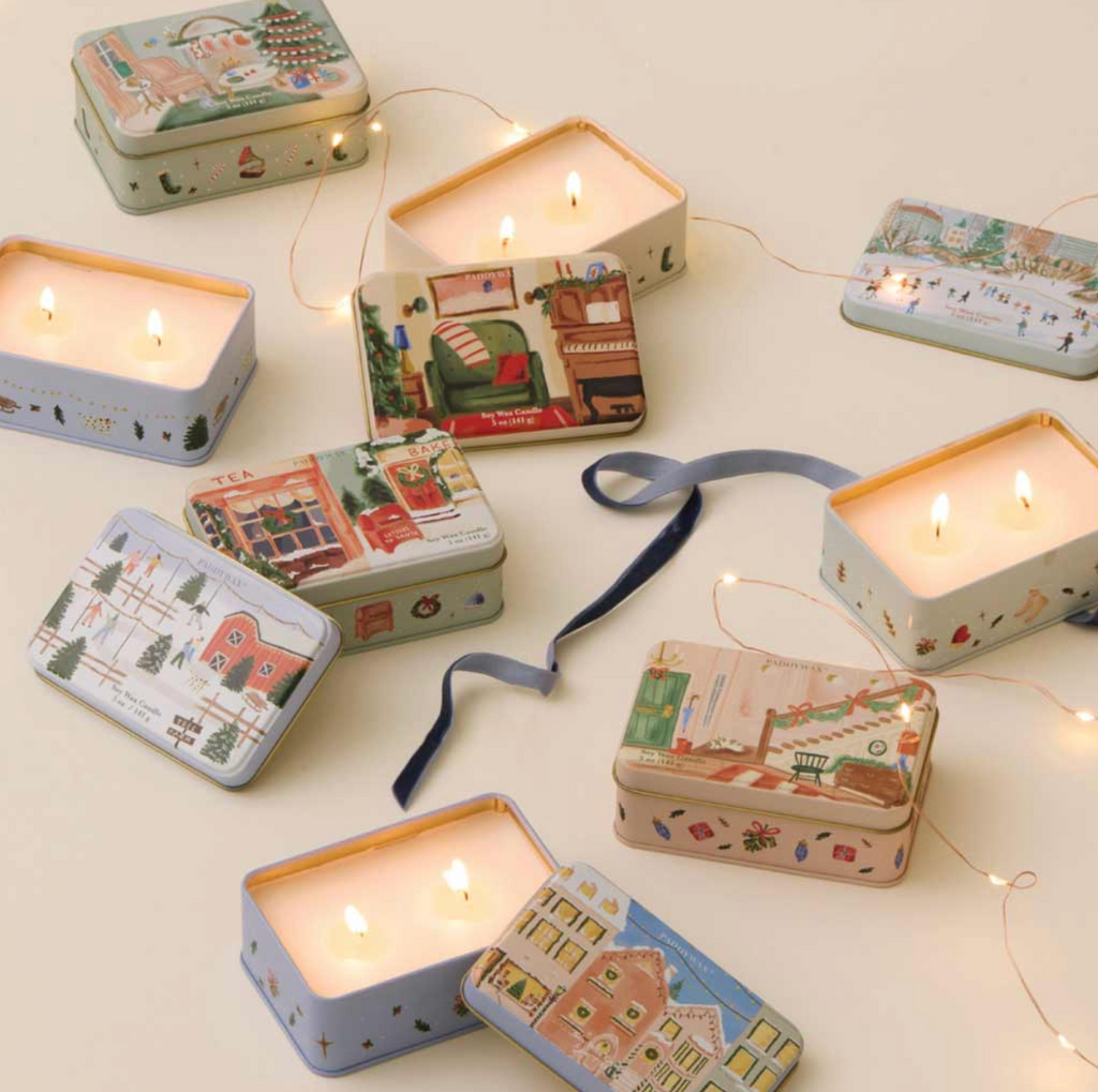 Decorative candles in tin boxes with illustrated lids on a light background