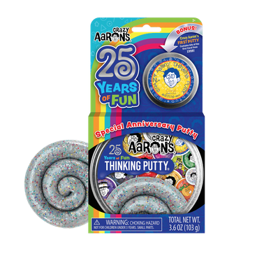 The Special 25th Anniversary Thinking Putty box with the tin inside and the putty itself beside the box. The box is bright blue and the tin has the silver glitter putty and labels from the last 25 years pictured on it. The putty beside it is silver with multiclored glitter mixed in. 