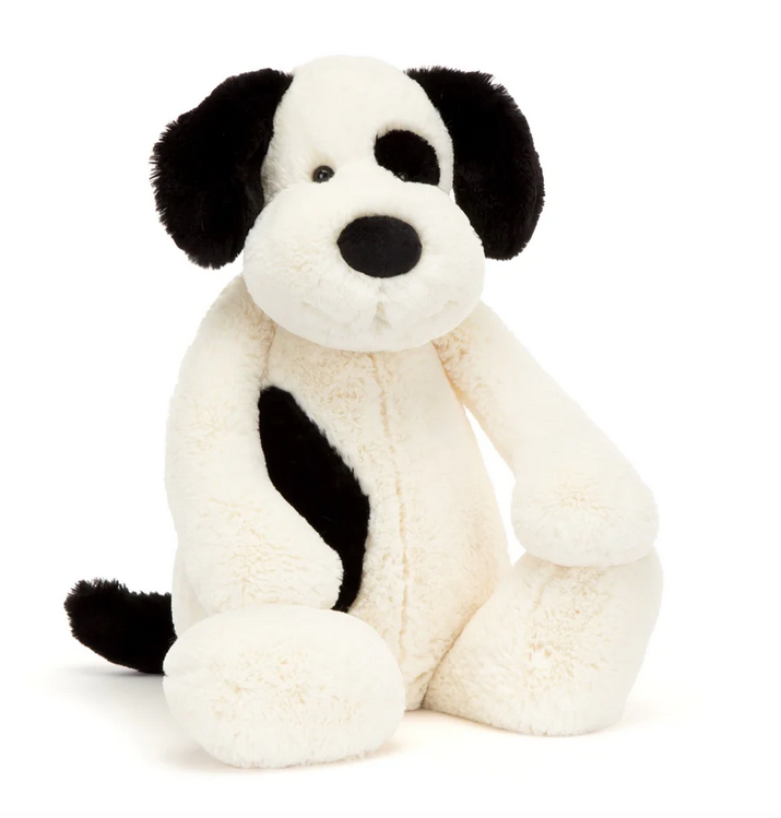 Really Big plush puppy with creamy fur and black spots here and there. He's sitting up and facing forward. 