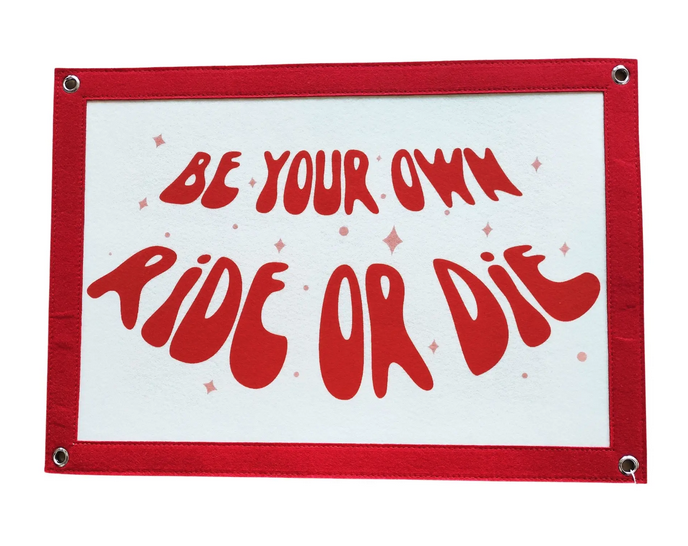 White felt banner that reads "Be your own ride or die" in red.