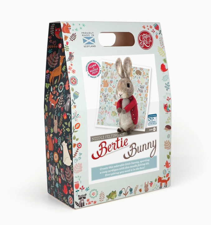The box for the Bertie Bunny Needle Felting Craft Kit with a picture of the felted Bertie Bunny wearing a red coat. The box has built in handles at the top and illustrations of animals and flowers down the sides of the box. 