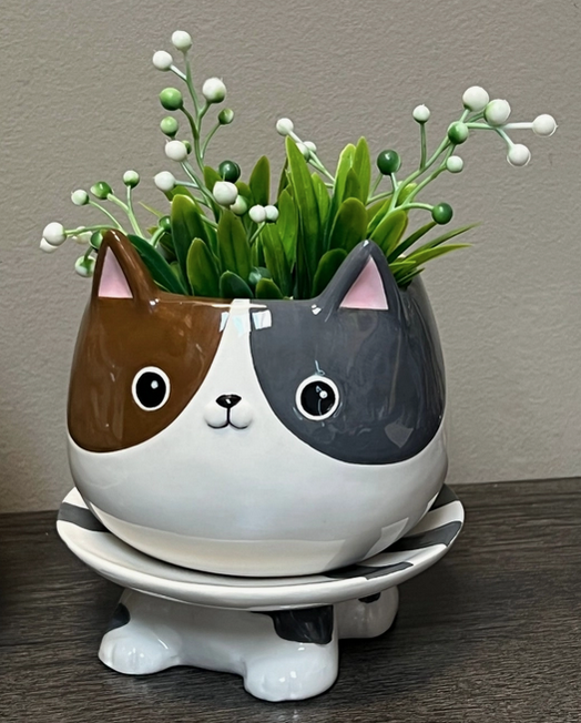 Grey and brown cat ceramic planter with artificial plant in it. 