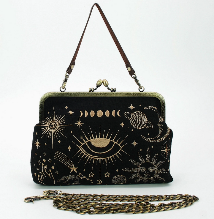 Black cloth purse with celstial themed embroidery in gold. Aged brass kiss lock hardware and a brown strap. The included aged brass chain strap  is in front of the purse. 
