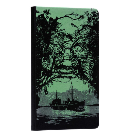 Glow in the dark cover of the Creature from the Black Lagoon journal. The creatures face is looming in the trees above a ship in the lagoon. 