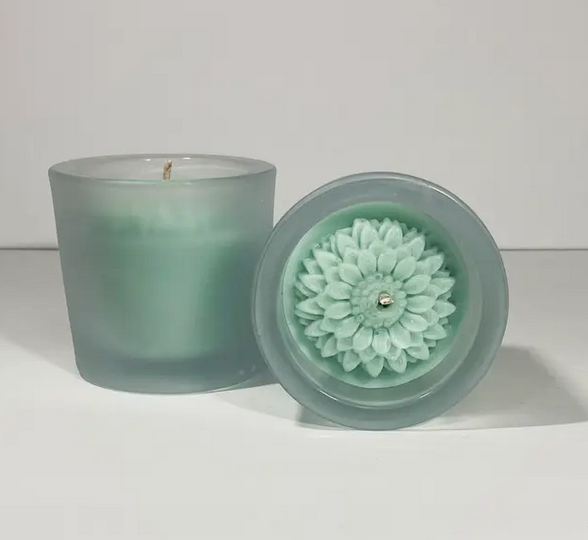 Two dahlia flower candles. One on it's side showing the flower and the other upright showing the frosted glass container. 