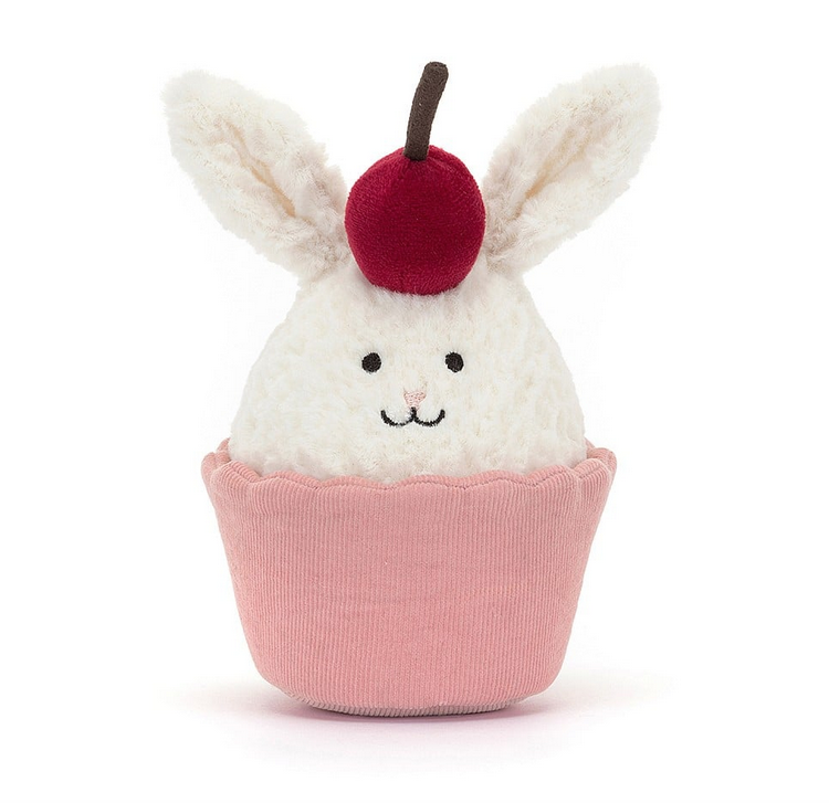 A cute cream colored bunny sitting in a pink cupcake with a cherry on top. 