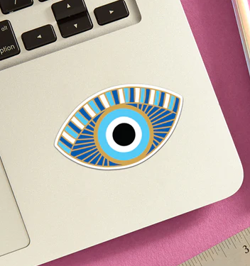 Evil eye die cut vinyl sticker. Colors are blue, turquoise, gold and white. Sticker is attached to the bottom corner of a laptop. 