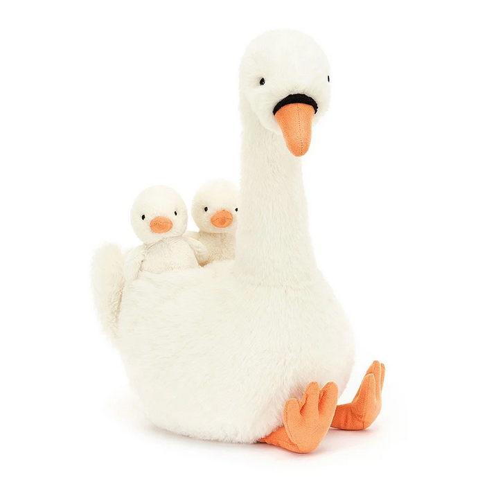 White plush Swan with orange webbed feet and beak. On her back are two baby swan ducklings. 