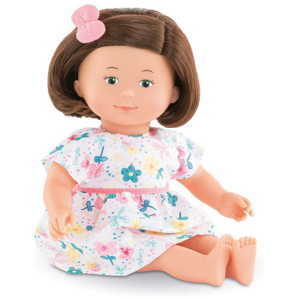 Florolle Églantine is 13-inch soft body doll shown here in a sitting position. She has silky, rooted hair styled in a bob, a playful look in her hazel painted eyes and a cheerful smile. Dressed in a floral-print dress and with a matching scrunchie in her hair. 