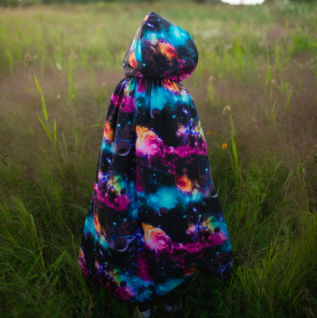 Child wearing galaxy cloak in a field.
