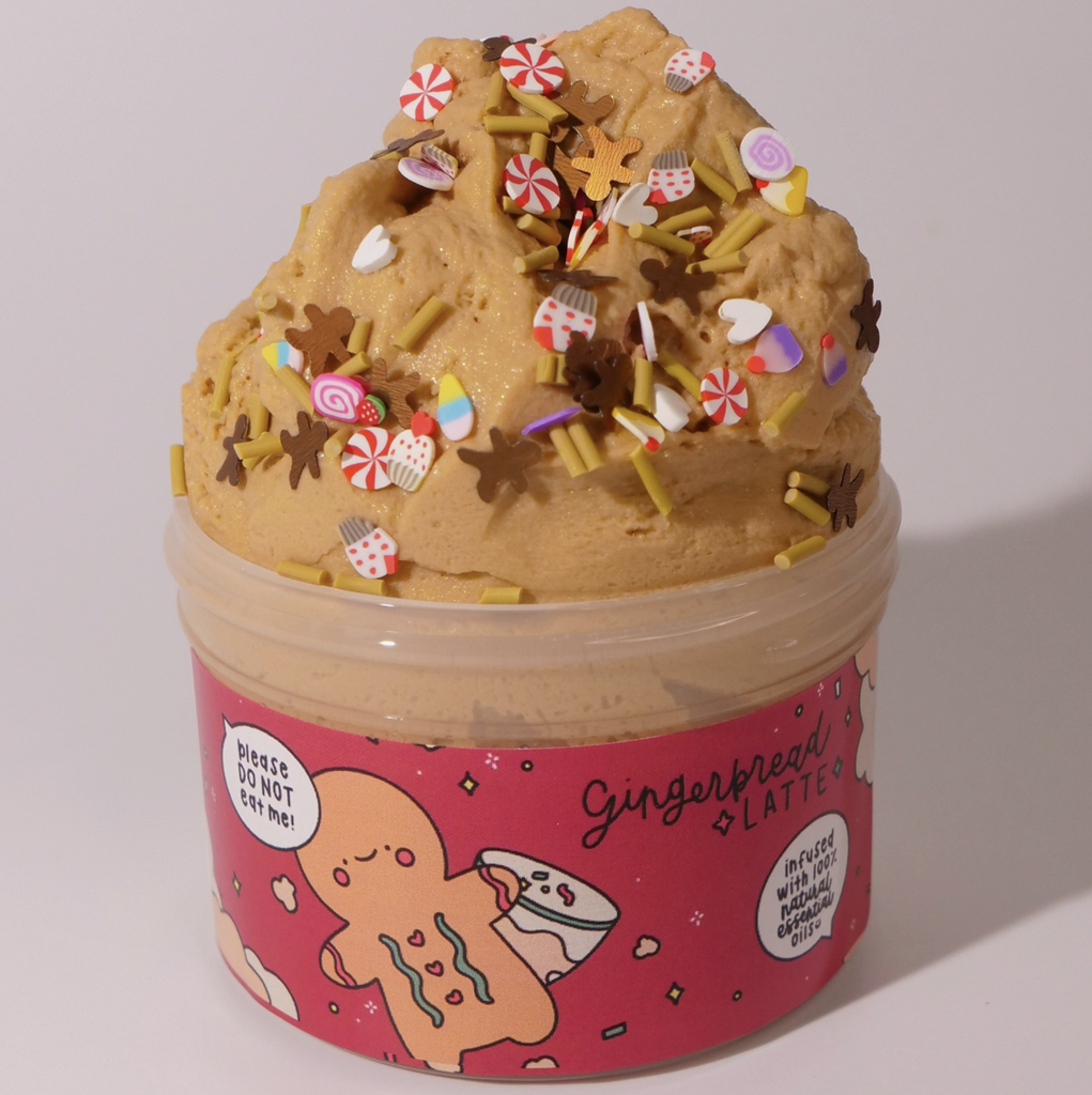 Gingerbread Latte Slime in an open jar. Slime is a little brown color topped with yellow sprinkles, pepermint shapes, gingerbread man shapes, and mitten shapes.