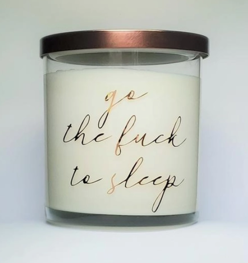 Glass candle that reads "go the fuck to sleep" in gold cursive.