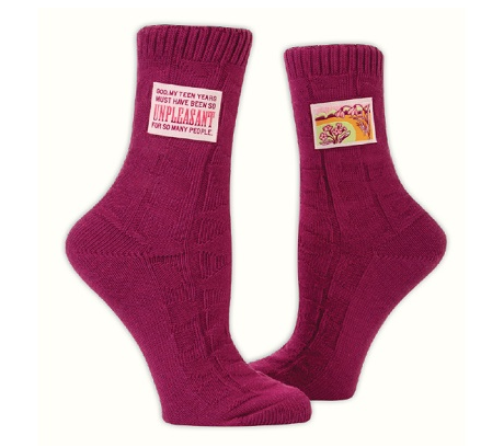Burgundy knitted socks with a patch at the ankle. POne reads "God, My Teen Years Must Have Been so Unpleasant For So Many People." Other patch shows garden flowers.