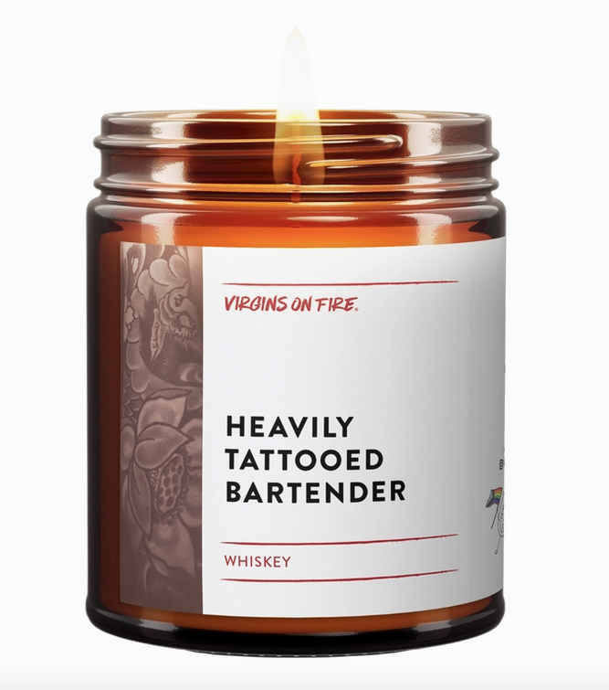 Soy wax candle in brown glass jar with flame. Wrap around white label with black lettering that reads " Heavily Tattooed Bartender" with illustration of floral tatto on the edge of the label. 