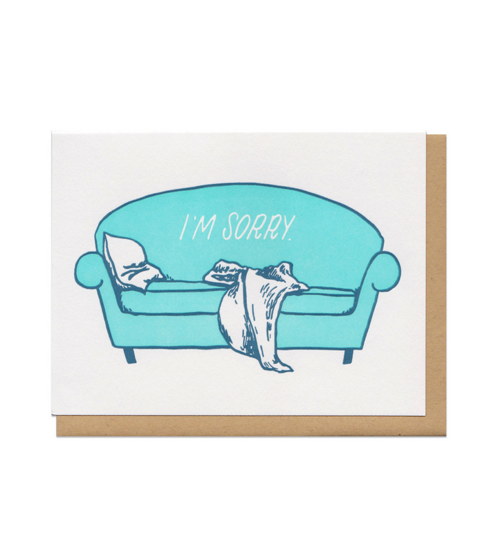 Letterpess press card of a blue couch with a white pillow and blanket that reads "I'm Sorry" in white text.
