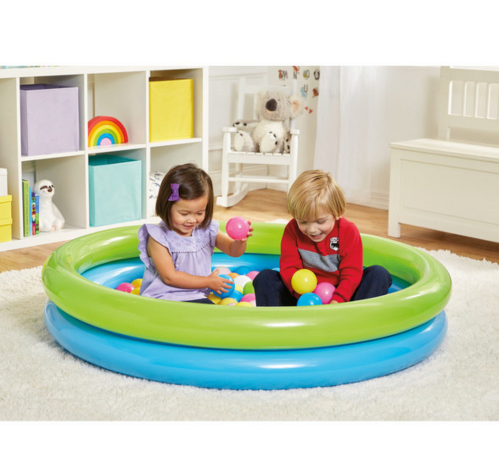 2 children in a room sitting in inflated pool and ball pit playing with colored balls.