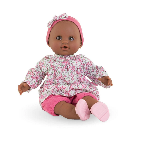 Lilou Doll is a black baby in a sitting position. Lilou is dressed in a floral top and pink trousers, and is also wearing a headband and ballet flats.
