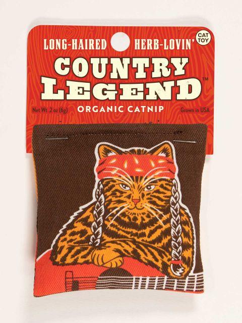 Front of catnip toy that is brown with an orange and brown cat with a red bandana and braids, who is also holding a guitar. The toy is attached to a red cardboard hang tag that reads " Long Haired Herb Lovin' Country Legend" in off white block letters. 