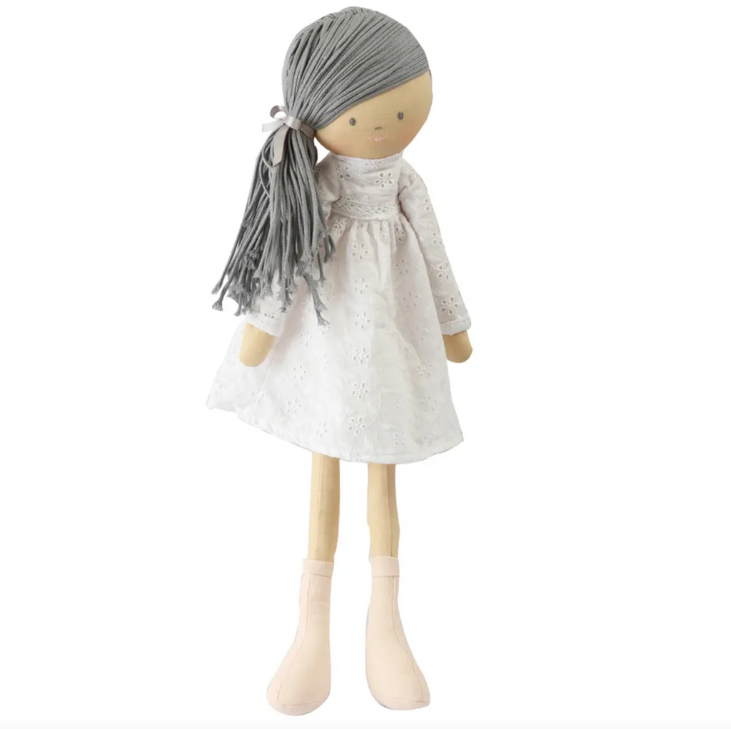 Oversize soft doll. Megan has long grey hair in a side pony and is wearing a long sleeved white eyelet dress.