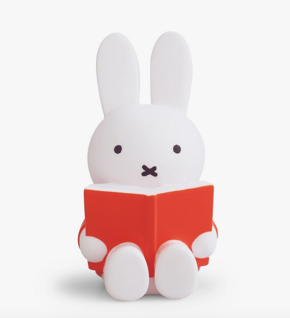 White Miffy figure coin bank sitting with a red book in her lap. 