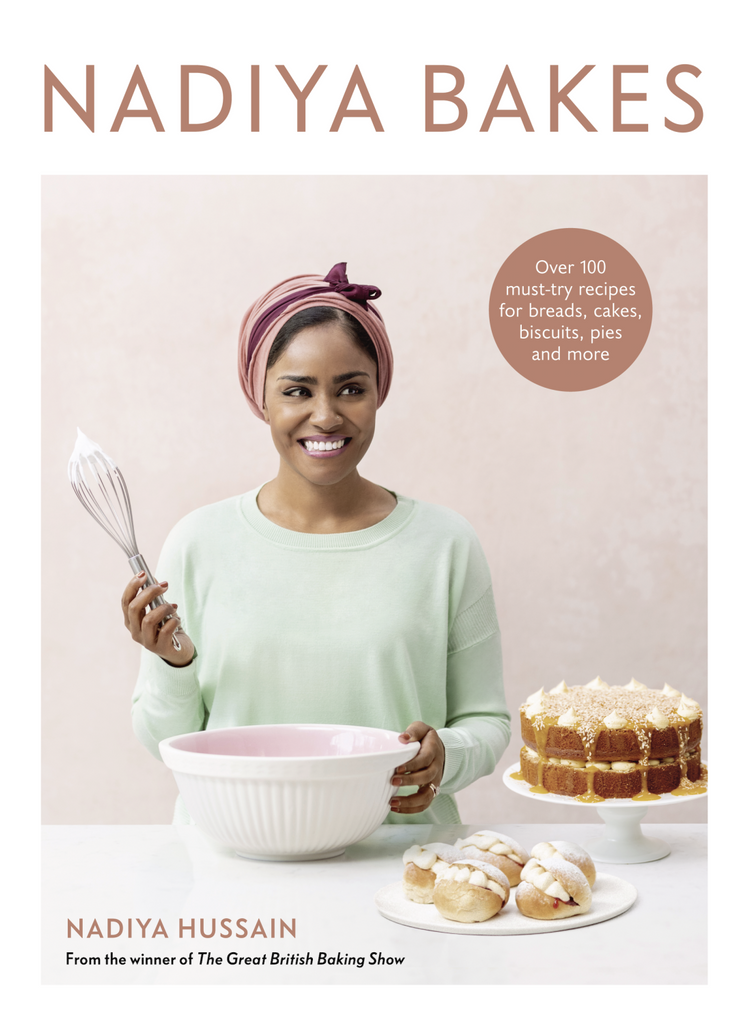 Cover of "Nadiya Bakes: Over 100 must try recipes for bread, cakes, biscuits, pies, and more" by Nadiya Hussain, winner of the Great British Baking Show. Photo of Nadiya smiling in a green shirt and pink headwrap holding a whisk behind a counter with a bowl and baked treats on top.