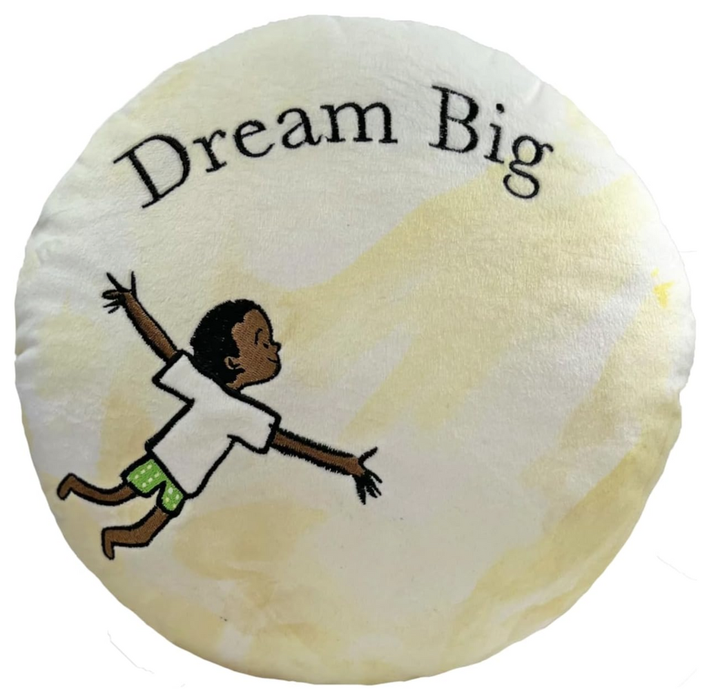 Round, creamy white and yellow plush moon with Nigel floating with his arms spread wide embroidered on it. The words "Dream Big" are also embroidered on it. 