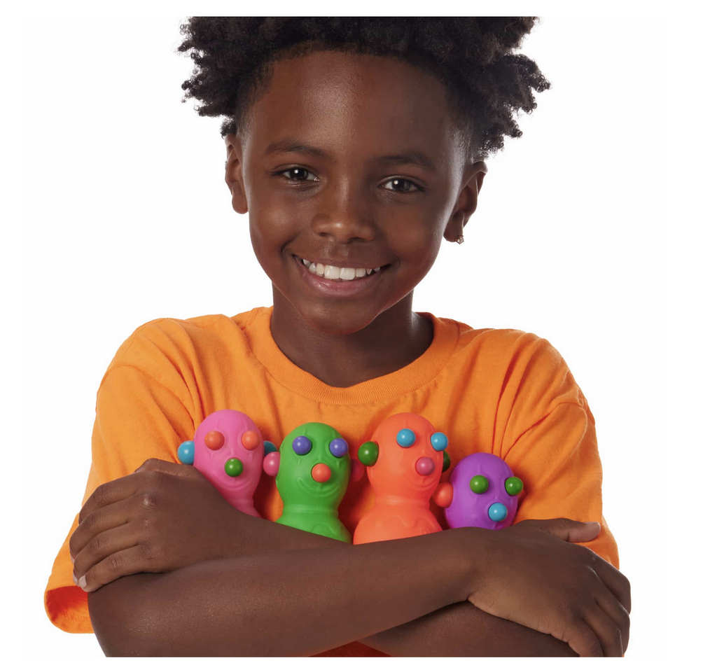 Smiling Black boy in a bright orange shirt hugging all 4 colors of the Panic Pete Needoh figures.