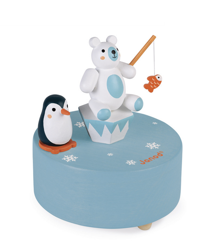 Polar music box. A white wooden polar bear sits on a wooden iceberg with a fishing pole. A wooden penguin sits nearby. Base is blue round wooden box that slowly spins as the music plays.