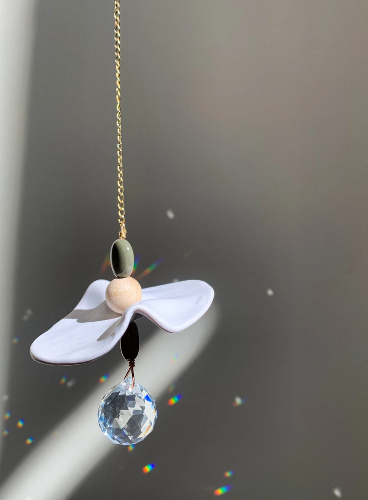 Clear prism hanging on a gold chain with gemstones, a white abstract shape, and a wooden bead.