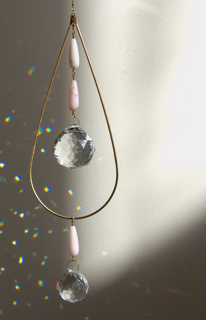 Gold chain with a gold teardrop shaped charm with a prism hanging from two pink stones inside and another prism hanging from a pink stone underneath.