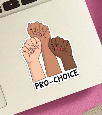 Vinyl die cut sticker with three fists in the air reading "Pro Choice". The fists are white, brown and black. The sticker is attached to the bottom corner of a laptop. 
