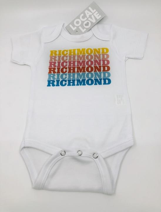 White baby onesie with Richmond repeating in sunset rainbow colors.