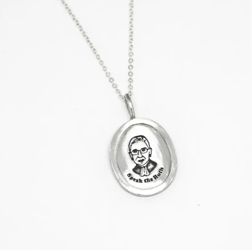 Silver chain necklace with an oval silver charm with a stamped image of Ruth Bader Ginsburg that reads "Speak the Ruth."