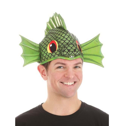 The Sea Monster Sprayzy hat has a printed scale pattern and is decorated with embroidered eyes. Stiffened green fish fins stick out above each ear, and another fin forms a top crest. In this picture an adult is wearing the hat. 