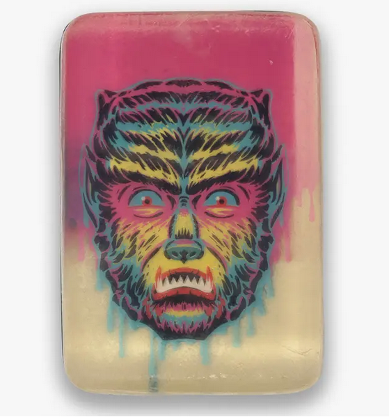 A multi-layered soap bar with a layer of black and white. It’s then topped with a clear layer featuring the full color "Shock Wolf" with blue, green amd electric yellow fur with a pink background. 