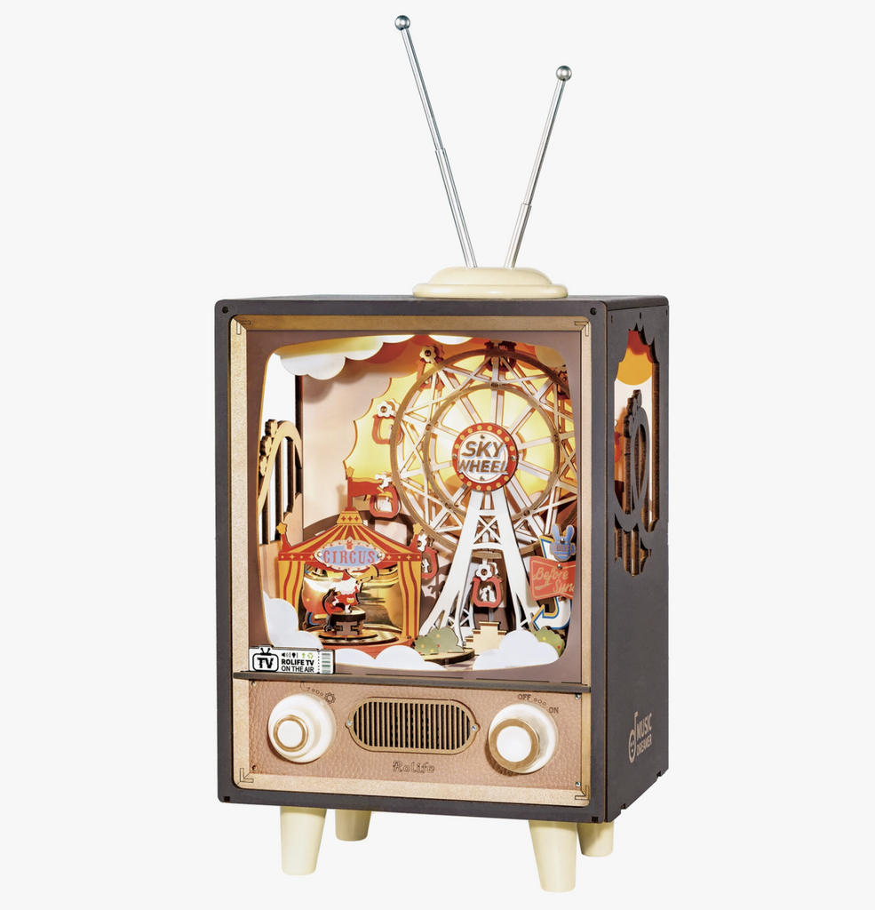 Sunset Carnival DIY Mechanical Music Box looks like a vintage tv with a 3d wooden screen scene of a carnival complete with a ferris wheel, circus tent, signs, lights, and more.