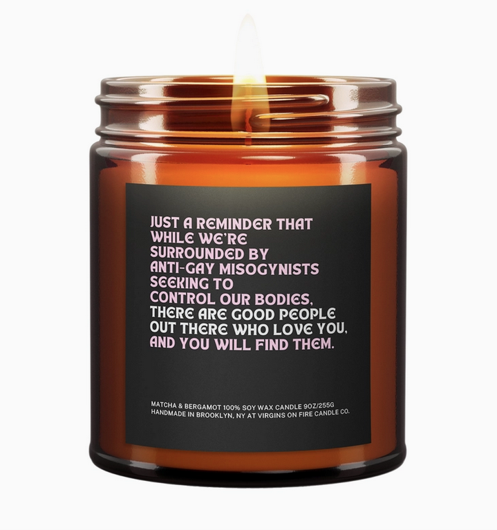 Soy wax candle in a brown glass jar with a black sticker label that reads " Just a reminder that while we're surrounded by anti-gay misogynists seeking to control our bodies, there are good people out there who love you. And you will find them. 