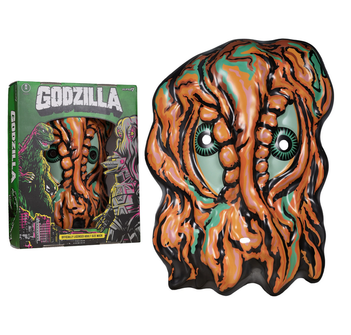 Hedorah mask and box. The smog monster mask is orange and green with eye and mouth holes. The box is green with Godzilla written in white block letters and illustrations of Godzilla, Hedorah and Mechagodzilla. 