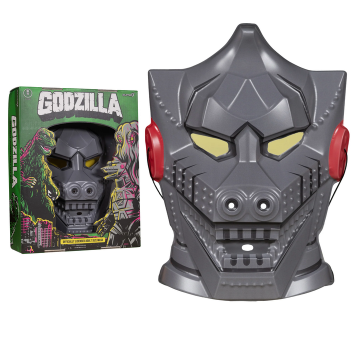 The alien mechanical wonder Mechagodzilla mask in mecha grey and box. The mask depicts Godzilla as a mechanical robot with a pointed head and red bolts at the ears. Has eye, nose and mouth holes. The box is dark green with white block letters that read Godzill. There are also illustrations of Godzilla, Hedorah and Mechagodzilla. 